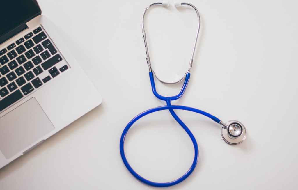 blue colored stethoscope next to a laptop computer on a white surface